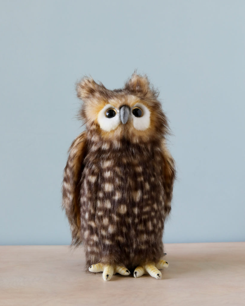A Owl Stuffed Animal with brown and white feathers stands on a wooden table against a light blue background. This high-quality Owl Stuffed Animal has large, round eyes and appears soft and fluffy.