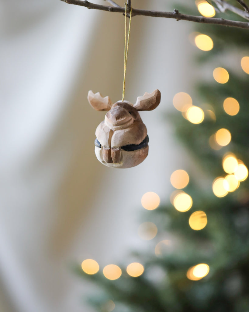 A hanging Wooden Ornament shaped like an owl, delicately carved in light brown with a twine loop, against a backdrop of softly blurred Christmas tree lights.