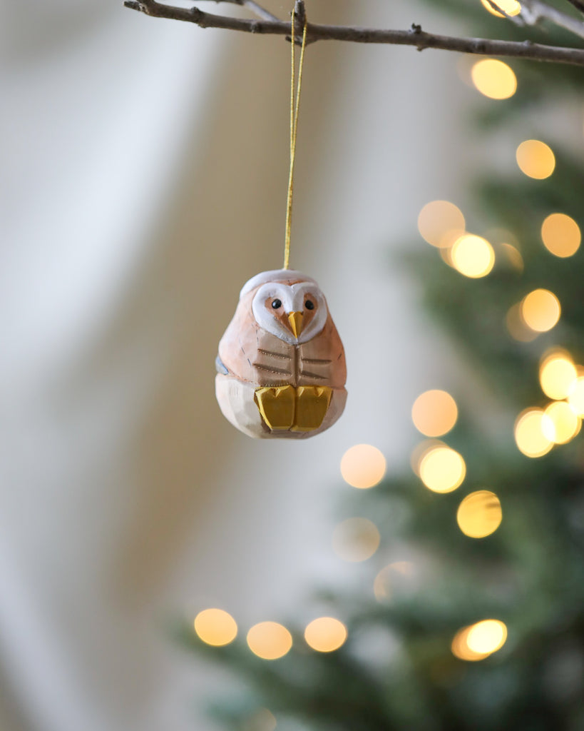 A wooden Christmas ornament in pastel colors shaped like a squirrel hangs from a tree branch, with softly glowing lights in the background.
