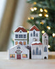 A charming holiday scene features a **Handmade Wooden Christmas Village** with small wooden houses, each painted with windows, doors, and a clock. One building is labeled "Book Shop." The background includes a blurred Christmas tree with warm lights, adding a festive atmosphere.