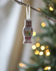 The Coral & Tusk Owl Ornament, with embroidered details, hangs from a branch, capturing the festive forest theme. In the background, warm white lights on a blurred Christmas tree add to the cozy holiday ambiance among other beautiful Christmas ornaments.