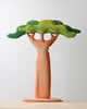 A minimalist artistic sculpture of the Extra Large Wooden Tree crafted from linden wood with a smooth trunk and stylized canopy in shades of green, set against a plain white background.