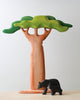 A small sculpture of an Extra Large Wooden Tree with a wavy green canopy and a smooth, beige trunk made from linden wood, next to a smaller black bear figure, against a plain white background.