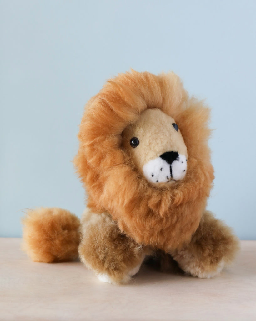 A Fluffy Lion Stuffed Animal sits against a light blue background. The lion has a gentle expression and its body is positioned facing the viewer.