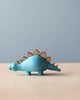 Sentence with product name: A Wooden Dinosaurs with a blue body and natural wood spikes along its back, set against a plain, light gray backdrop. This piece makes an ideal pre-historic decoration.