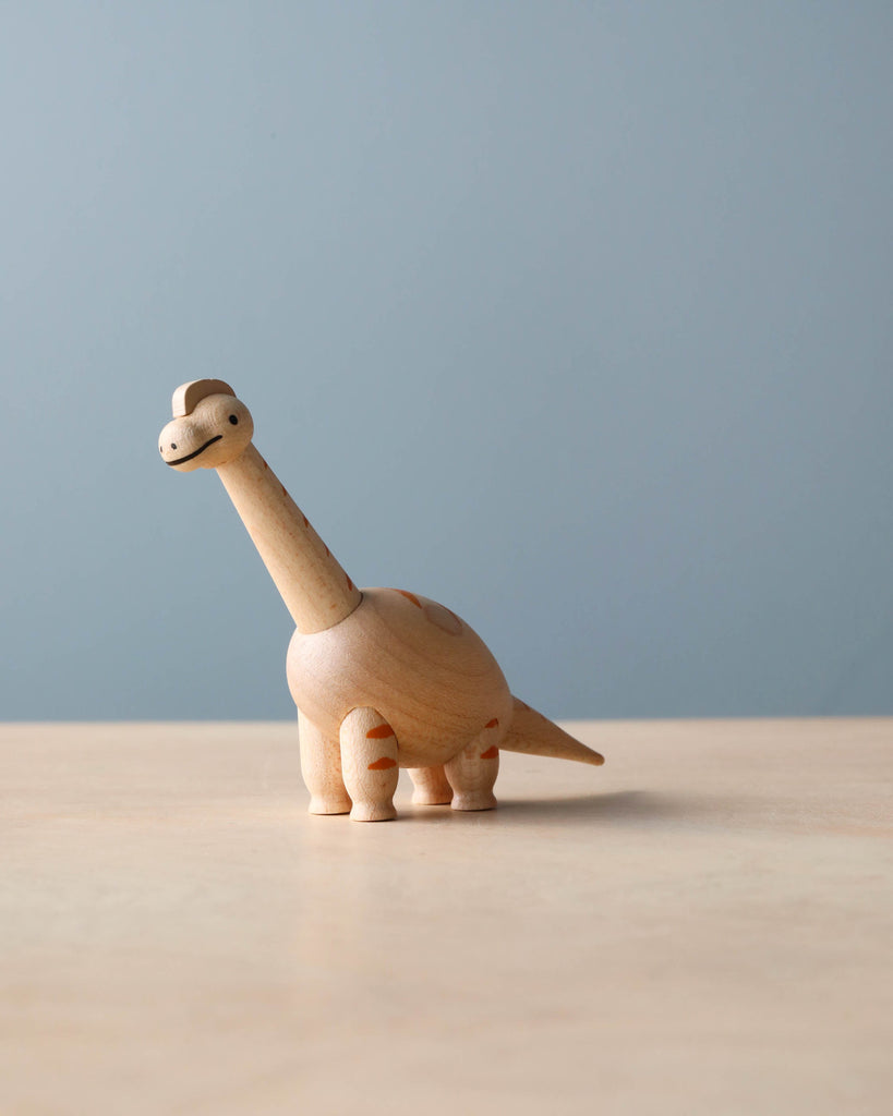 A Wooden Dinosaurs set on a table, featuring a long neck and tail, placed against a soft blue background.