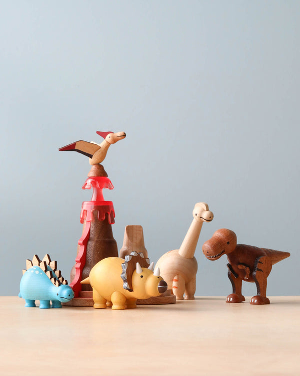 A collection of Wooden Dinosaurs on a table, each uniquely crafted and painted, featuring a variety of species including a stegosaurus and a t. rex, perfect as an aspiring paleontologist