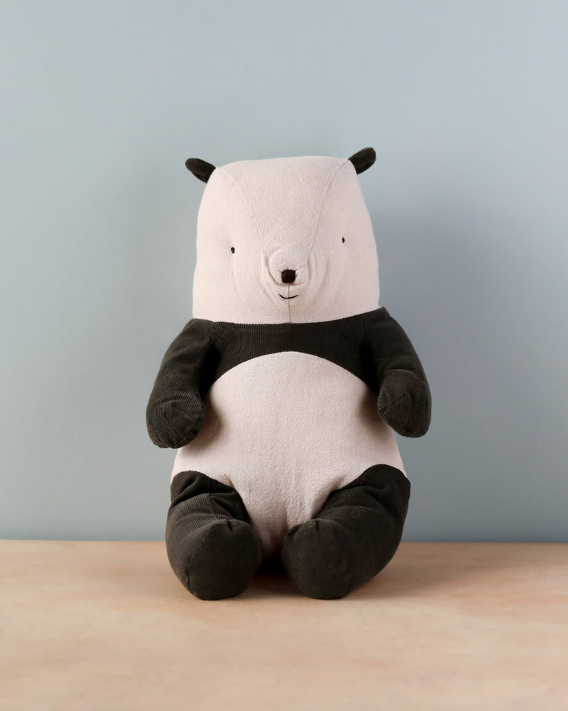 A Maileg Panda Stuffed Animal sitting upright against a soft blue background. The toy has a smiling face, dark ears and limbs, and is made of cuddly polyester cotton.