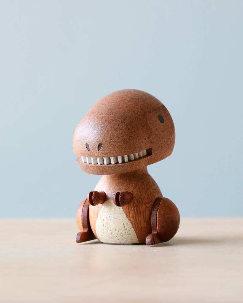 A Wooden T-Rex Bobblehead with a smiling face, round body, and prominent teeth, sitting against a soft blue background. Its texture is smooth with visible wood grain.
