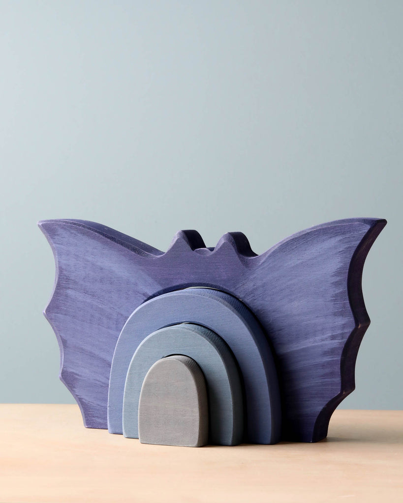A set of purple wooden bat-shaped nesting shelves, crafted from non-toxic dyed poplar hardwood, on a wooden table against a pale blue background.
