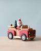 A Santa-mobile Music Box, crafted from premium hardwoods and painted red and beige with white wheels, carries charming wooden figures: a snowman driver, a small Christmas tree, and a puppy in the back.