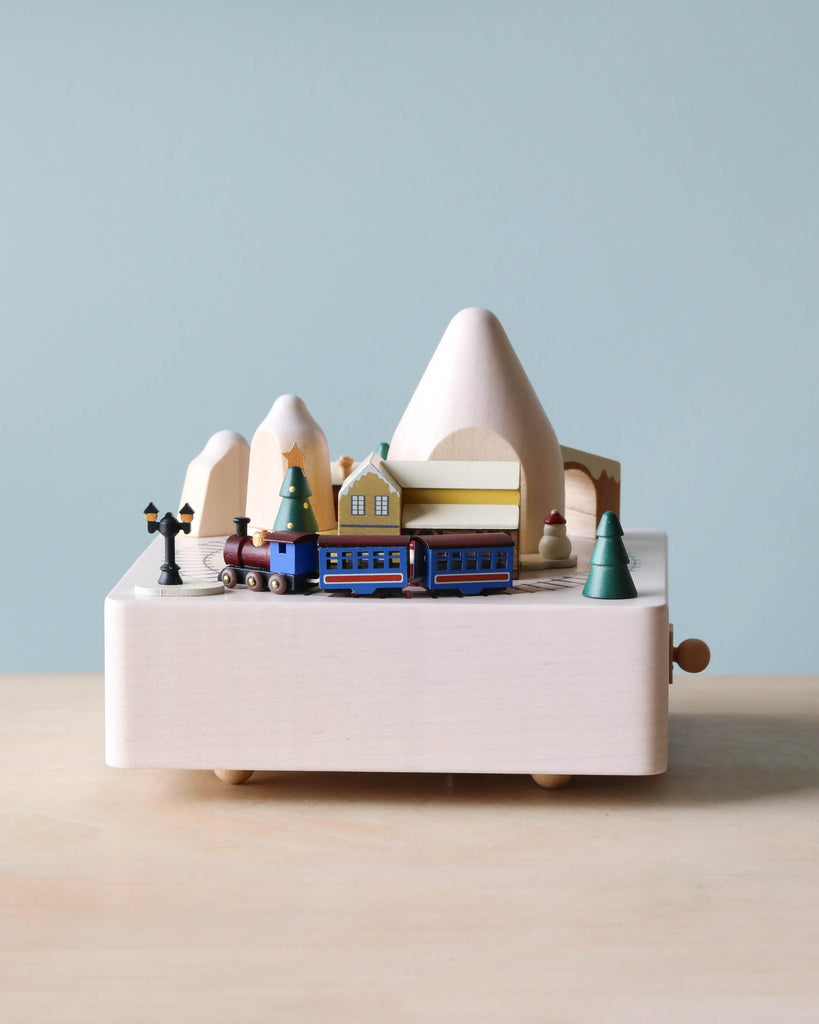 A Christmas Train Music Box miniature toy scene with mountains, houses, and trees against a plain blue background.