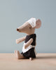 A small, beige Maileg Maid Mouse dressed in a black, classically maid outfit with a white apron and headpiece sits on a wooden surface against a plain, light blue background. The mouse, perfect for any housekeeping theme, is positioned in profile, facing left.
