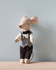 A small plush toy mouse, affectionately called the Maileg Waiter Mouse, is dressed in formal attire with a black and white houndstooth vest, white shirt, black bow tie, and black pants. Equipped with magnets in hands for added charm, it stands upright on a wooden surface against a plain light blue background.