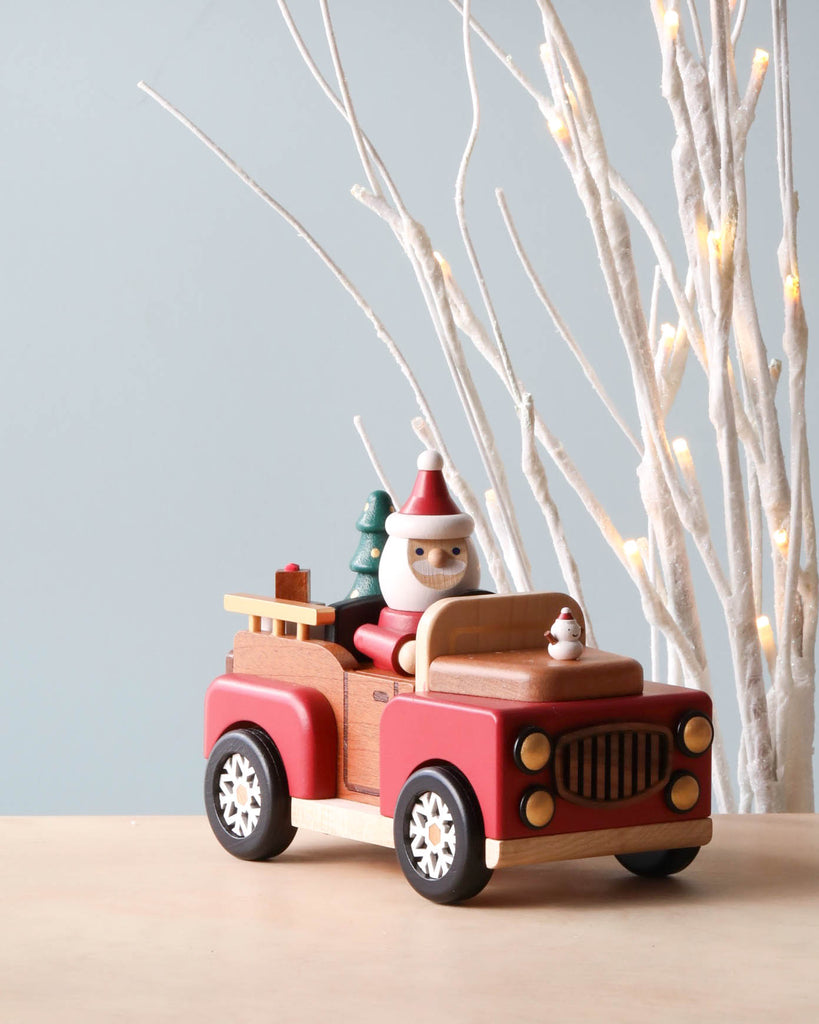A Santa-mobile Music Box crafted from premium hardwoods with a cartoon-like design, painted in red and beige, carrying two whimsical figurines resembling a nutcracker and a gnome, set against a neutral background.