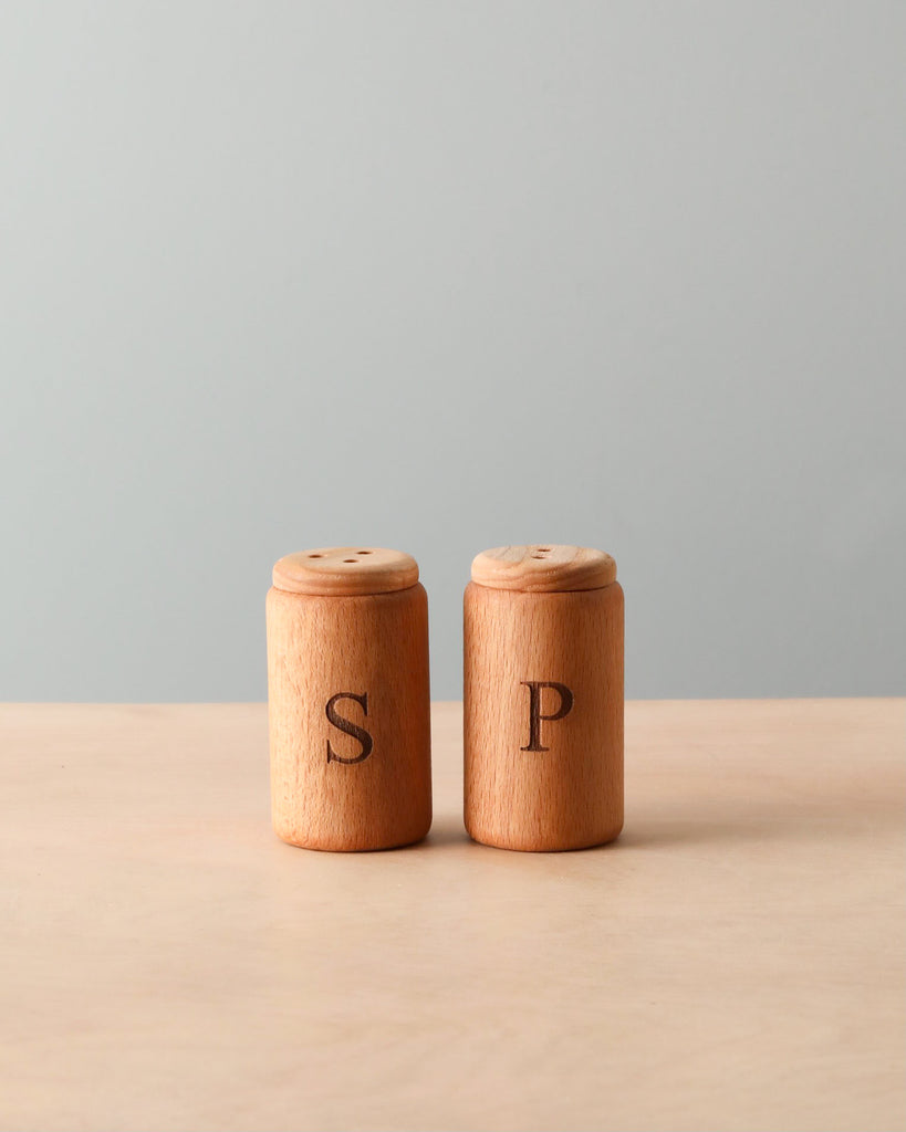 Wooden pretend play salt and pepper shakers standing next to each other. Natural color counter and light blue background. 