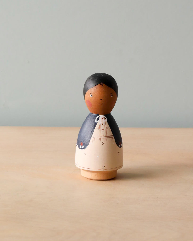 A handmade Peg Doll - Mom with a simplistic design, painted with a peaceful face, dark hair, and wearing a blue and white kimono, standing against a plain, light grey background.