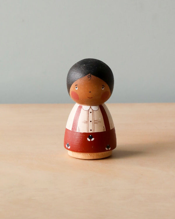 A Handmade Peg Doll - Girl With Braided Hair with hand-painted features, wearing a striped red and white shirt, displayed on a wooden surface against a plain light gray background.