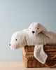 Two Senger Naturwelt Cuddly Animal - White Seal toys, one larger and one smaller, handmade in Germany, laying on top of a woven wicker basket against a soft blue background.
