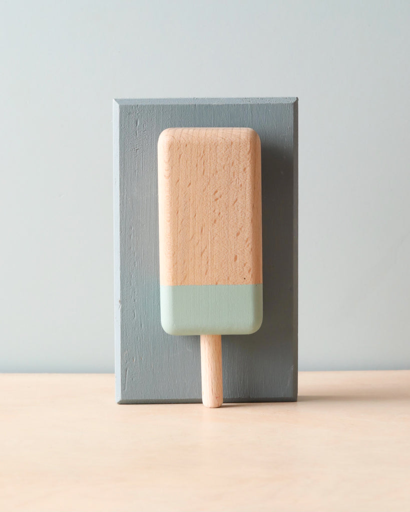 Wooden handmade natural color and blue popsicle (blueberry flavor). Leaning against light blue wooden block. 