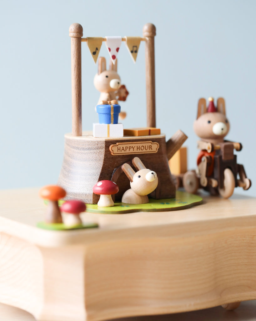 A whimsical Wooden Bunny Music Box from Wooderful Life, featuring anthropomorphic animal figures, including a rabbit bartender and a squirrel with a wheelchair, adorned with decorative mushrooms and a "happy hour" sign.
