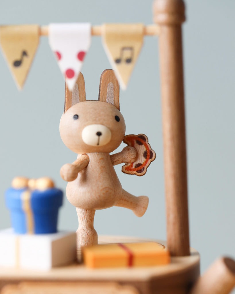 A Wooden Bunny Music Box featuring a wooden figurine of a rabbit holding a pretzel, standing on a platform with other small items and a banner adorned with musical notes and a heart above.