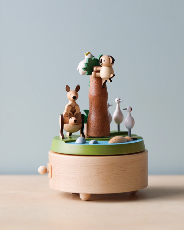 A sustainably sourced Wooden Australian Safari Park Music Box featuring whimsical animal figures, including a panda, kangaroo, and birds on a tree, against a soft blue background.
