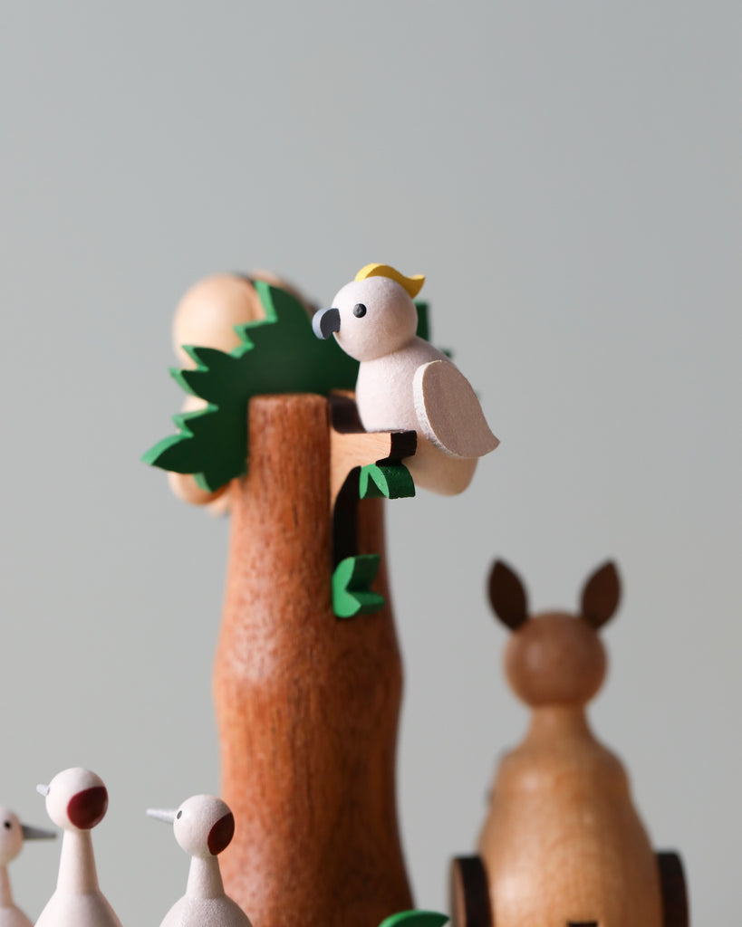 A Wooden Australian Safari Park Music Box with a white bird with a yellow tuft on its head perched on a tree, crafted from sustainably sourced wood, accompanied by other animal figurines, against a plain background.