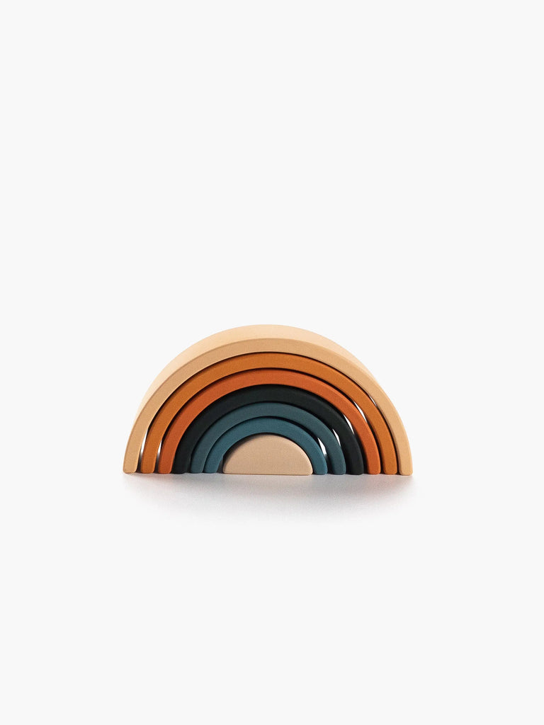 A stack of Handmade Mini Rainbow Stacker - Tropics toy pieces in various shades from light brown to dark teal, arranged to form a semicircle, against a white background.