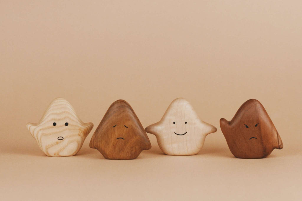 Four small Wooden Ghost Emotions, treated with natural linseed oil, stand in a row against a beige background. From left to right, they express basic emotions: neutral, sad, happy, and angry.