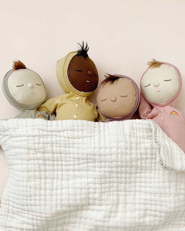 Four soft dolls with different skin tones in pajamas under a gauze blanket. 