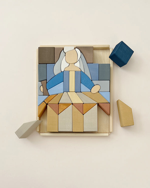 A wooden puzzle resembling an abstract figure with a blue and grey theme, partially assembled on a beige background. Some Raduga Grez Infante Blocks are detached beside it.