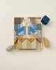 A wooden puzzle resembling an abstract figure with a blue and grey theme, partially assembled on a beige background. Some Raduga Grez Infante Blocks are detached beside it.