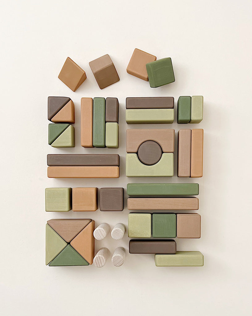 The Handmade Wooden Building Blocks are crafted from linden wood and come in various shapes and earthy tones, such as green, brown, and beige, all arranged neatly on a light background. They're ideal for enhancing fine motor skills.