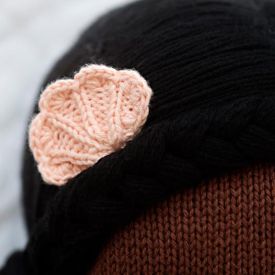 Close-up of a person wearing a black Cuddle + Kind Maya the Mermaid hand knit hat and a brown Cuddle + Kind Maya the Mermaid hand knit hat underneath, decorated with a small, pink crocheted flower on the side.