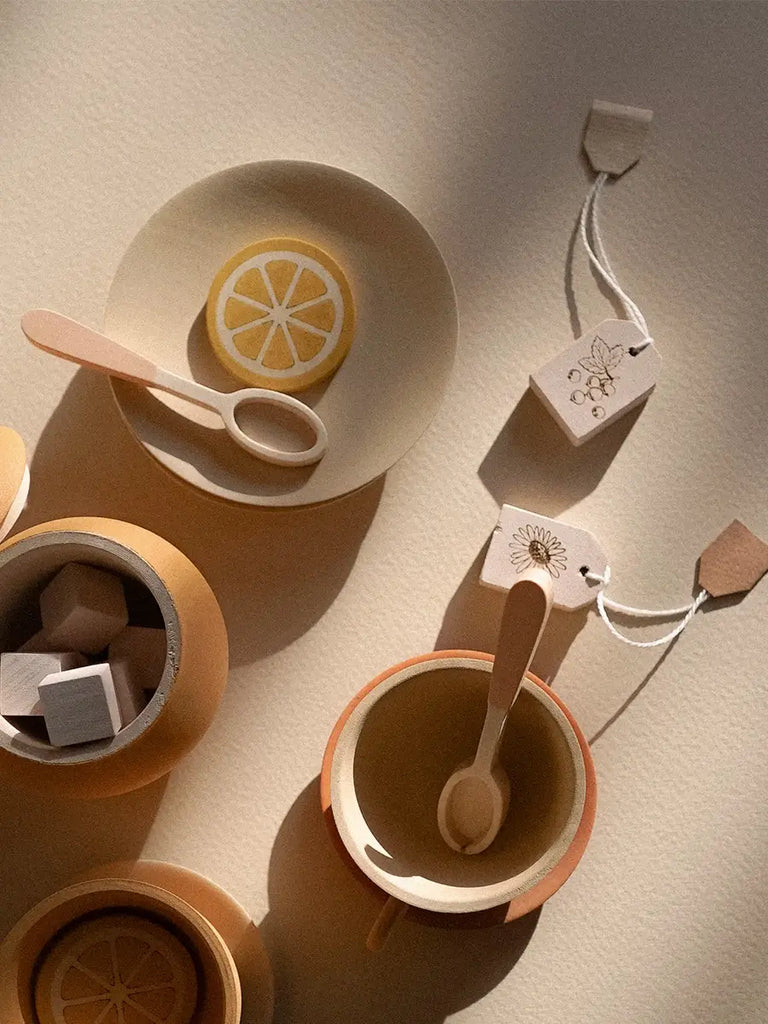 Abstract arrangement of ceramic dishes and a Handmade Wooden Tea Set - Flower with subtle shadows on a textured surface, featuring circular patterns and slices of citrus.