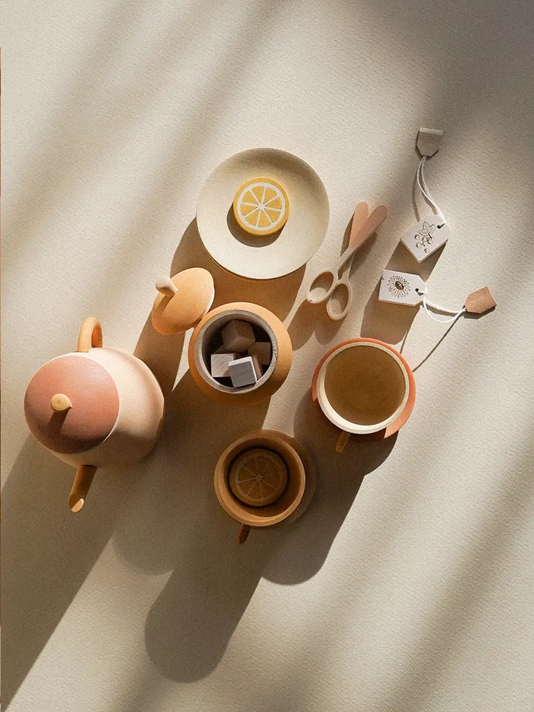 A top view of a collection of elegant ceramic tableware items in soft pastel colors, including a Handmade Wooden Tea Set - Flower, artistically arranged with sliced lemons, shadowed by natural light.