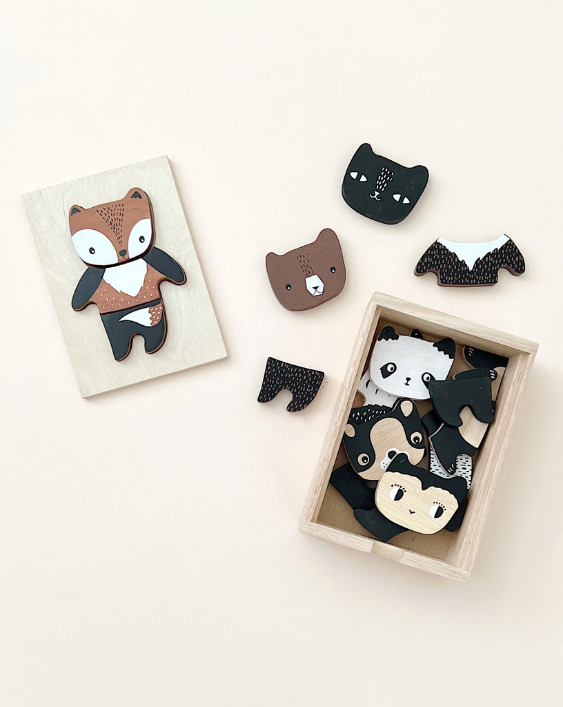 Wooden toys shaped like animals, including a nearly completed fox and Mix & Match Animal Tiles forming other animals, arranged next to a box on a light background.