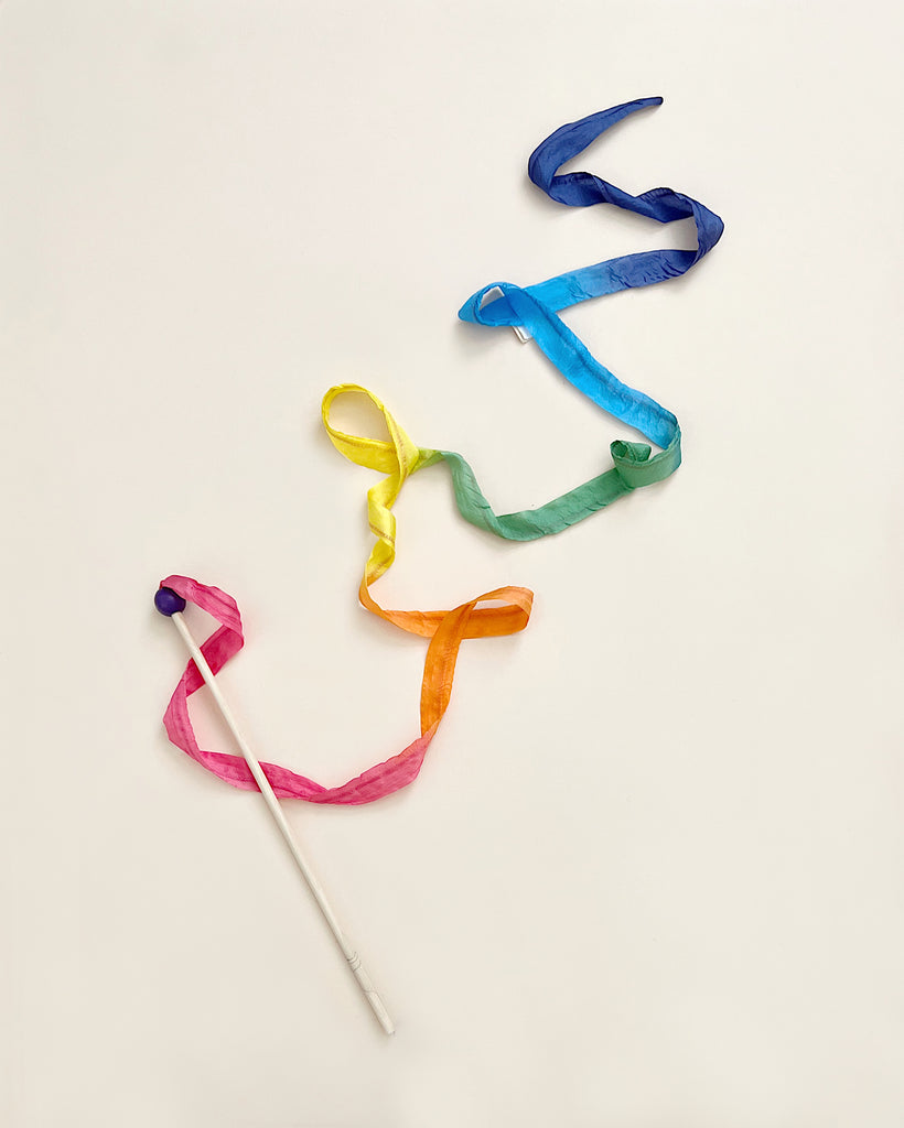 A white rhythmic gymnastics Sarah's Silk Rainbow Streamer Wand with its Rainbow Streamers artistically arranged on a light background to form a flowing, abstract shape.