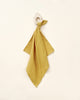 A Organic Muslin Lovey with a knotted loop hanging against a light beige background, handmade in Spain.