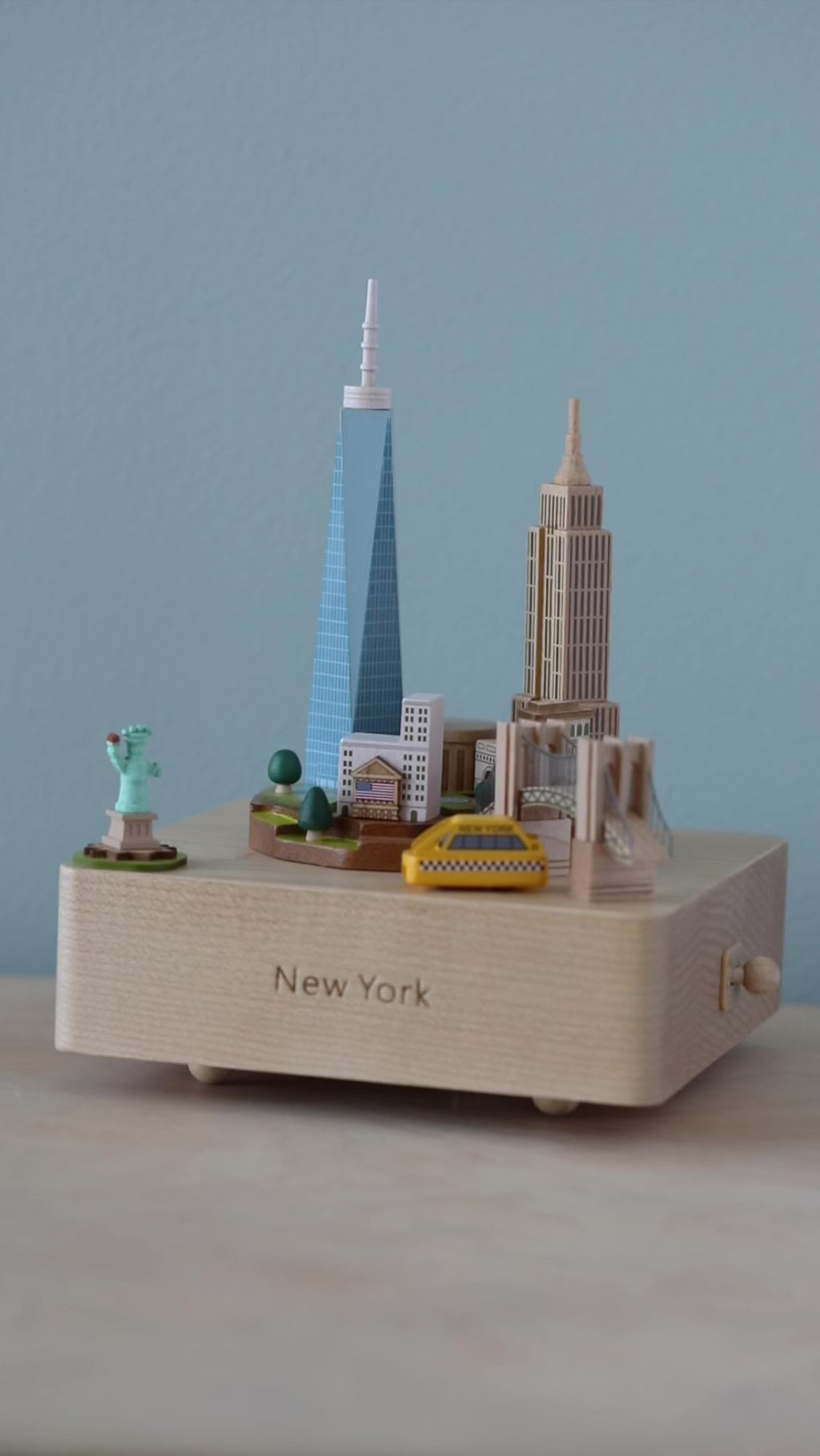 Video of a wooden music box showing a landscape of New York City with Statue of Liberty in the corner and taxi going around. 