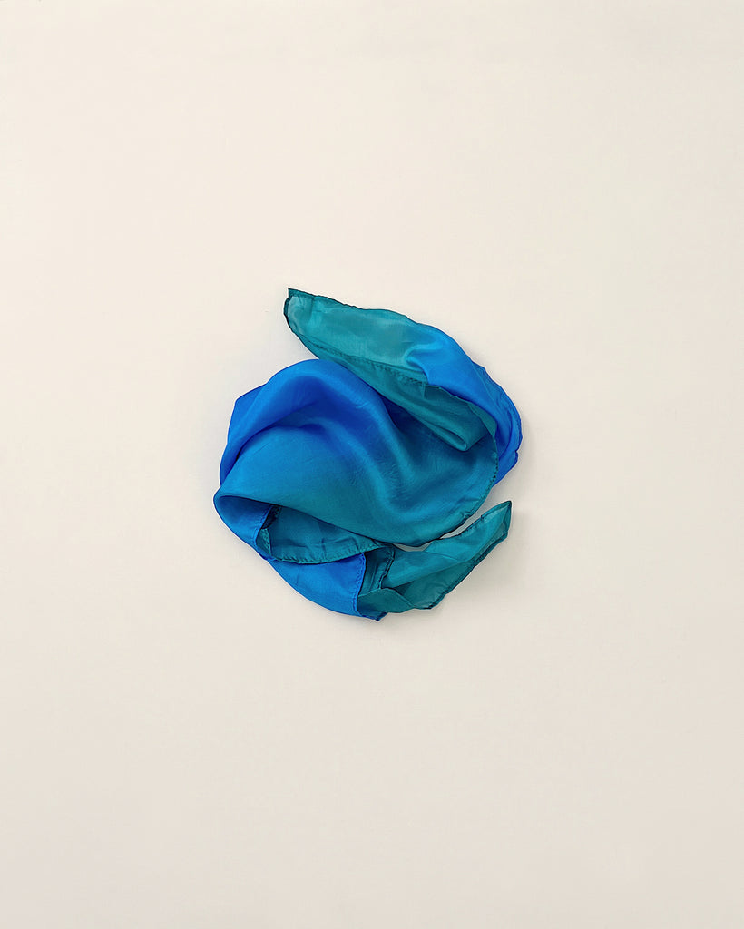 A crumpled turquoise Sarah's Silk Playsilk - Ocean arranged in a loose, imaginative shape on a plain white background.