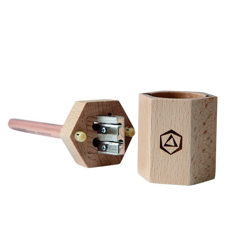 A Stockmar Dual Pencil Sharpener, specifically a pitch pipe, made from FSC certified lime wood with a hexagonal body and copper tube, next to its cylindrical wooden case featuring a black diamond symbol.