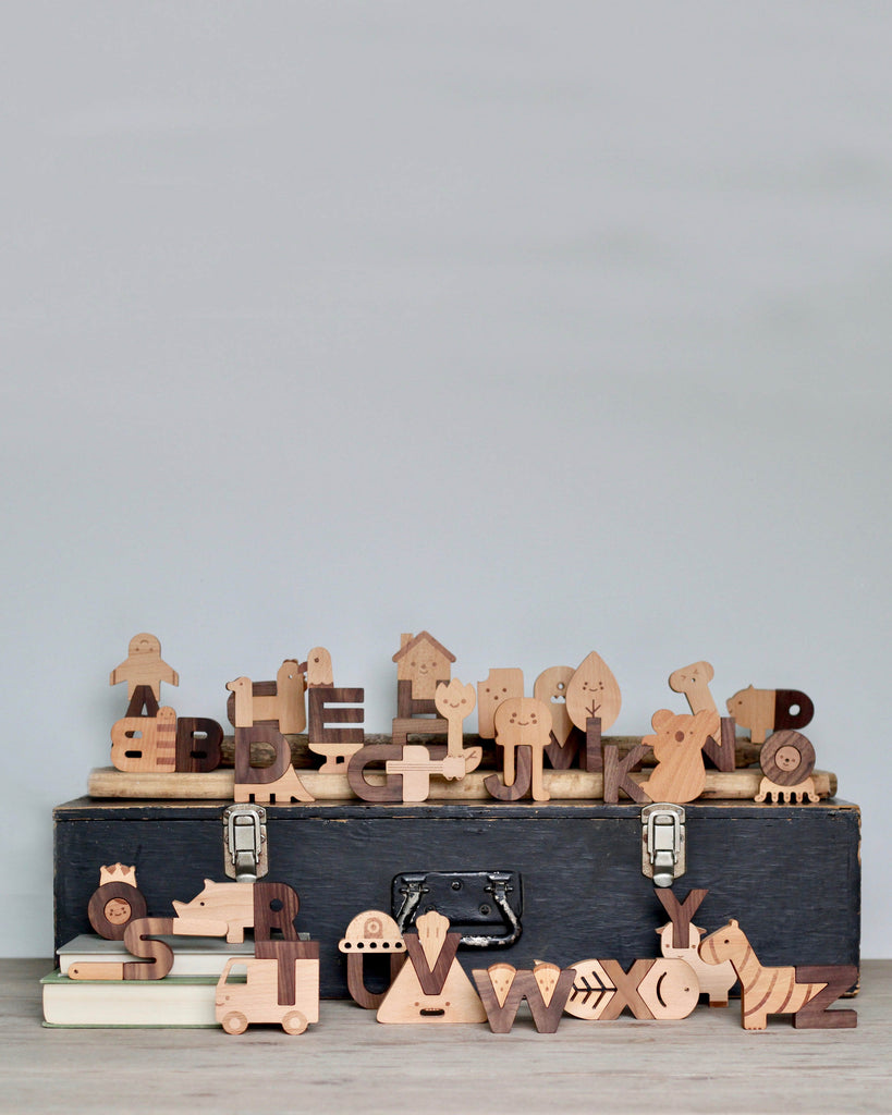 A collection of Ultimate Wooden Alphabet Puzzles, neatly arranged on and around a vintage suitcase against a plain gray background.
