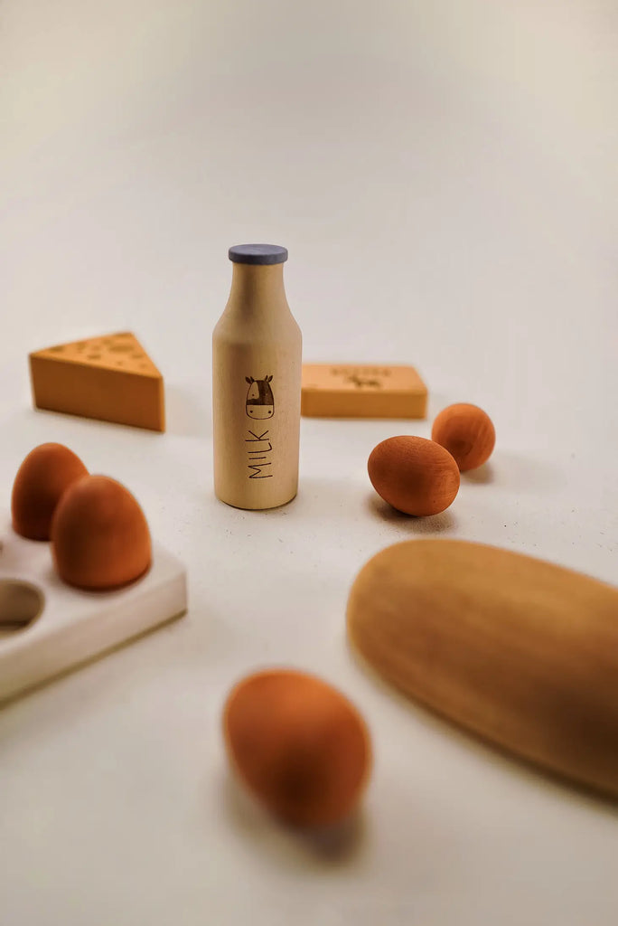 A minimalist still life arrangement featuring a small, Sabo Concept Handmade Wooden Dairy Set surrounded by wooden objects including educational toys, a spoon, and geometric shapes on a soft beige background.