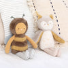 Two plush toys, a bee and an Owl Stuffed Animal, sit beside a striped cushion on a cozy blanket, crafted in Vietnam, displaying a charming and comforting aesthetic.