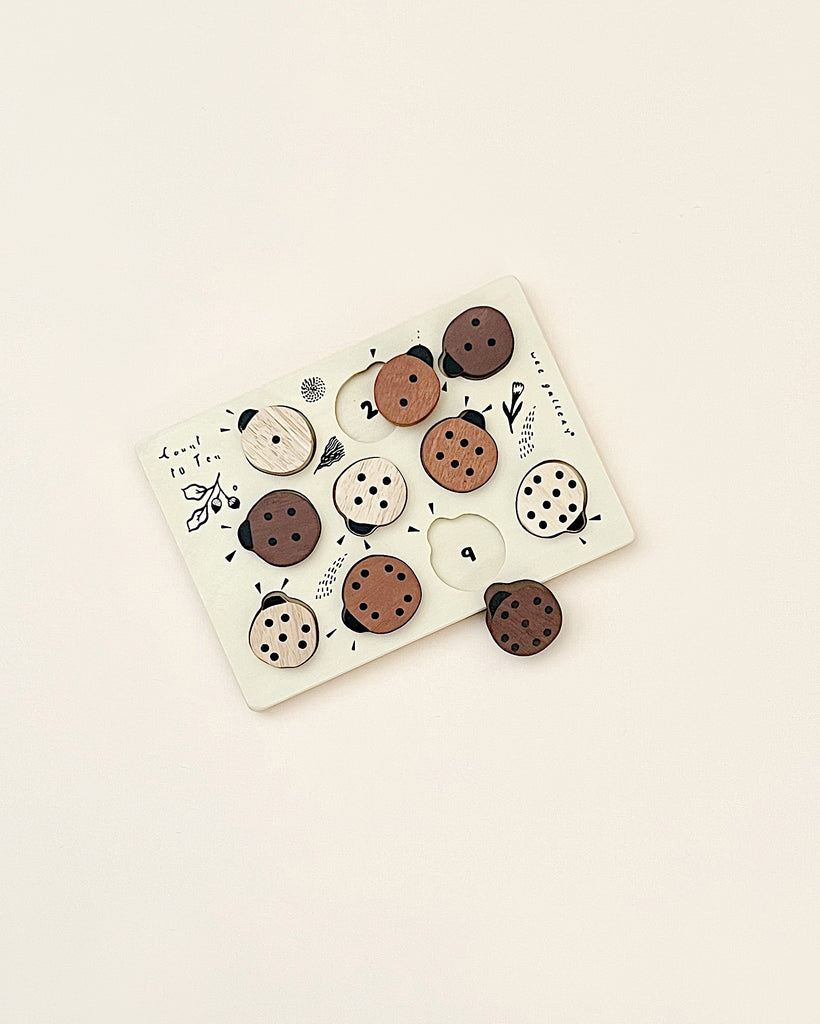 A Wooden Tray Puzzle - Count to 10 Ladybugs featuring various round animal faces and shapes in black, white, and natural wood colors on a soft beige background, crafted from sustainably sourced rubberwood.