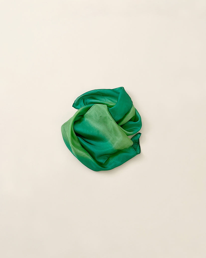 A crumpled, vibrant green Sarah's Silk Earth Playsilk - Forest is lying on a plain, light beige background.