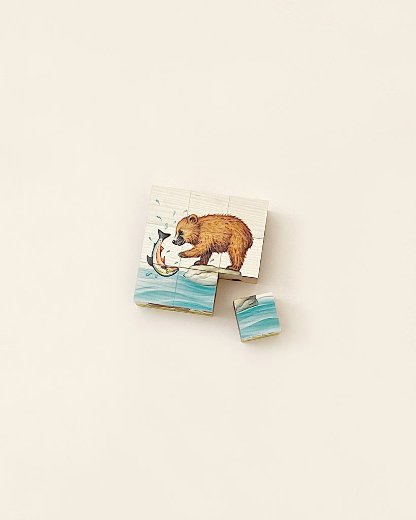 A partially assembled Wooden Block Puzzle - 9-Piece Bear on a plain background, depicting a brown bear catching a fish in its mouth, with a few scattered puzzle pieces nearby.