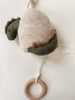 The Lullaby Activity Pull Toy - Dinosaur is crafted from soft lambswool, featuring a beige body, green limbs, and a brown crest. It has a pull string attached to a wooden ring at the bottom to activate a music box that plays "Twinkle Twinkle Little Star." The toy is placed on a white background.